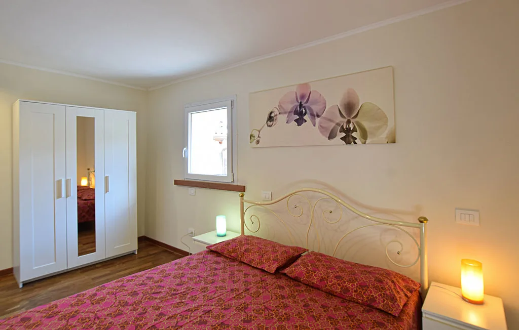 A bedroom with a patterned bedspread, white wardrobe, and floral wall art.