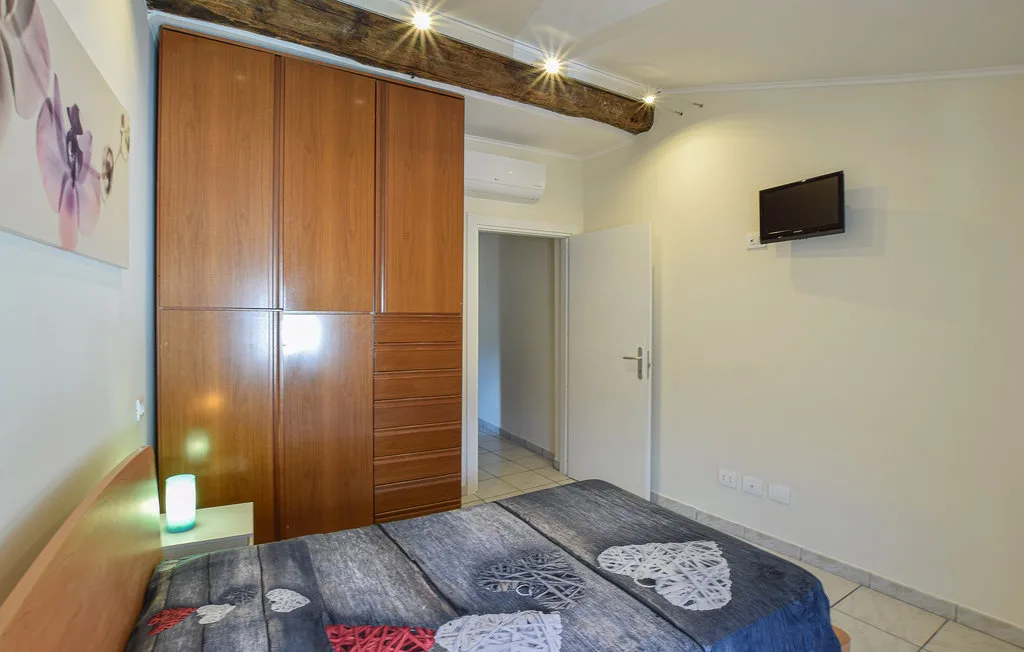 A bedroom with a wooden wardrobe, beds, and a wall-mounted television.