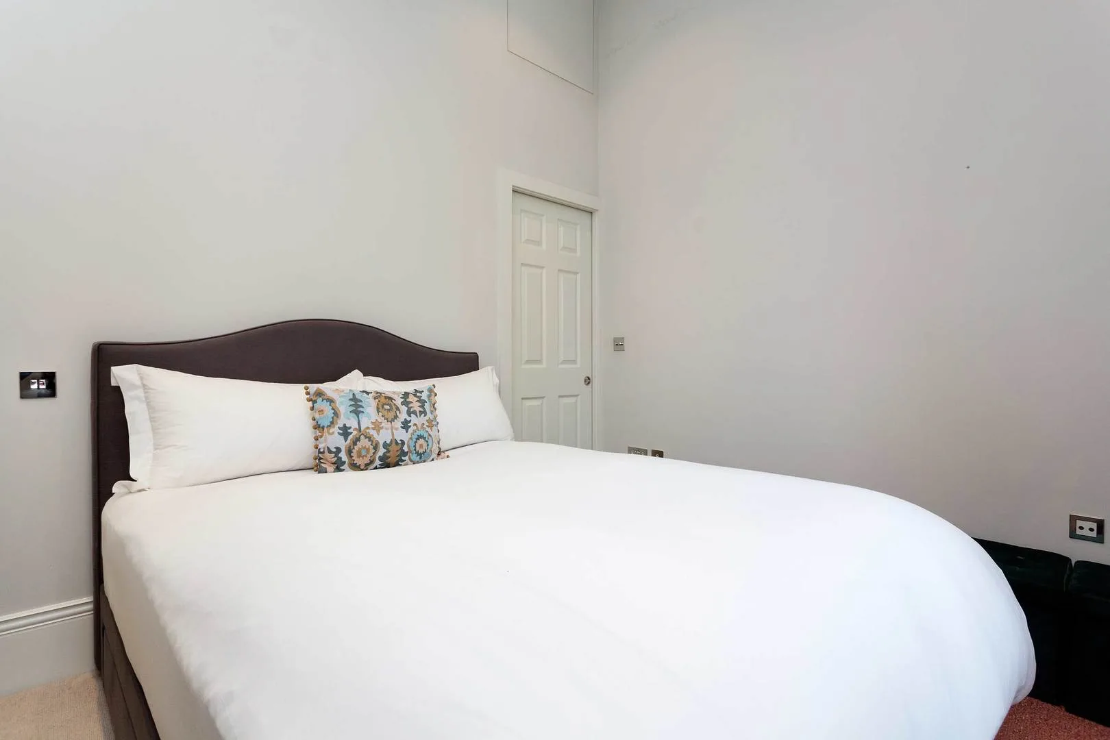 Un dormitorio con una cama vestida de blanco y un cojín decorativo estampado.