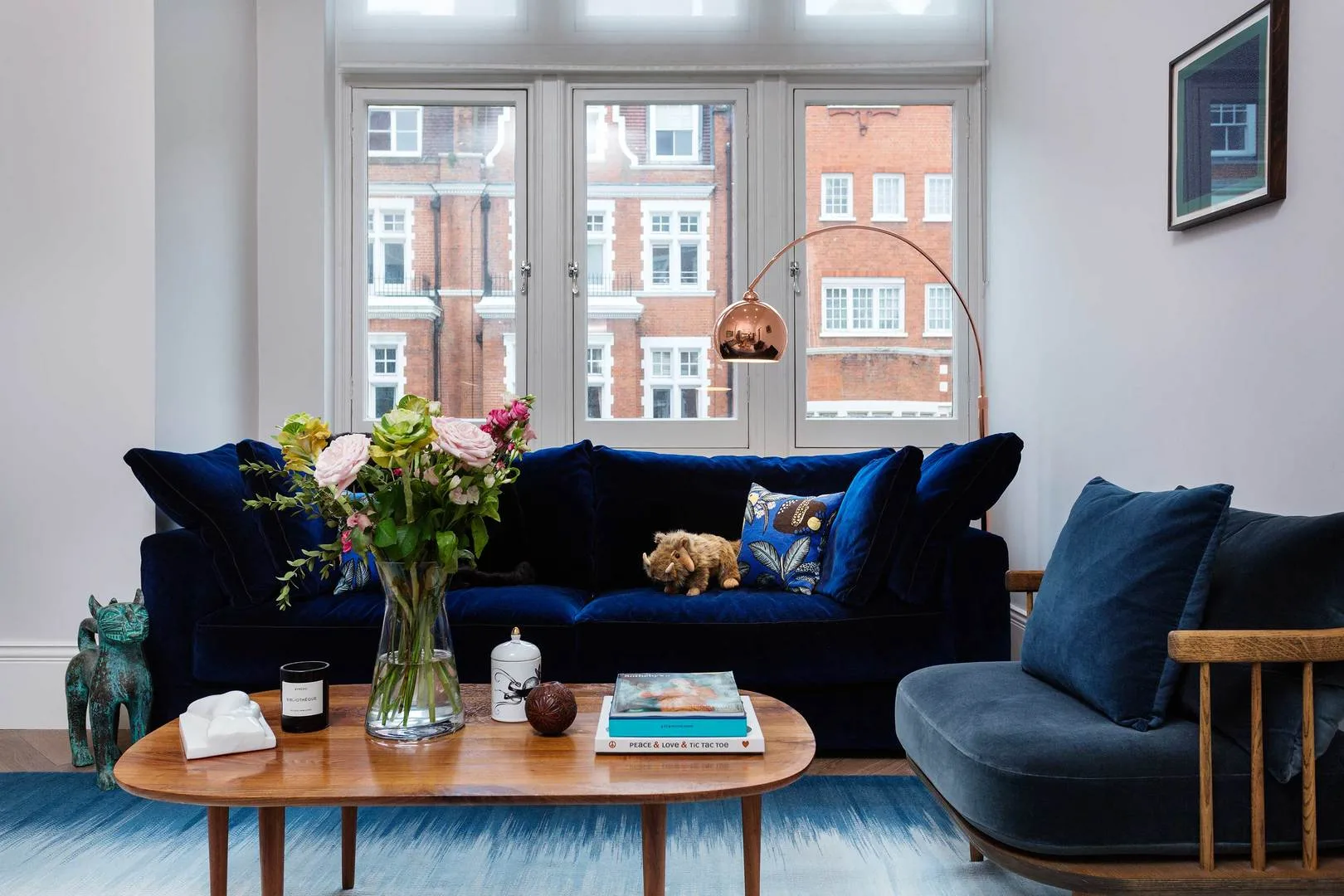 Una sala de estar con asientos azules, una mesa de centro de madera y ventanas grandes.