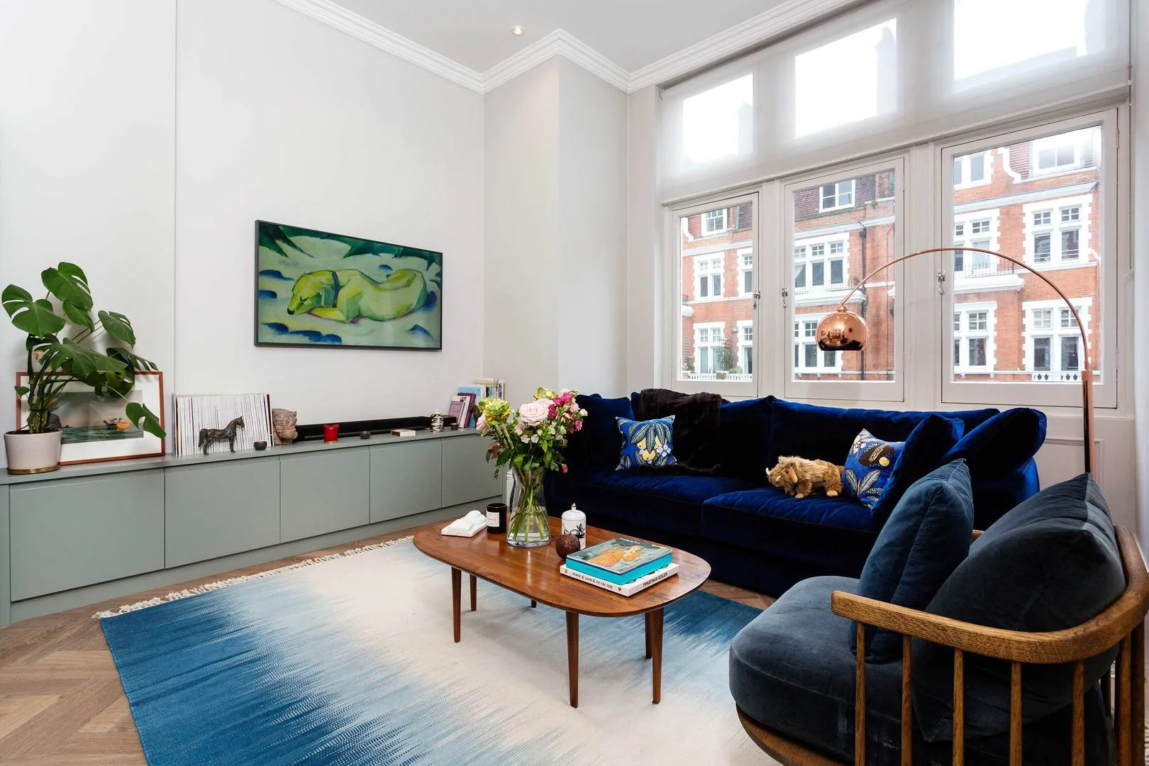 Una sala luminosa con un sofá azul, ventanas grandes y una mesa de centro.
