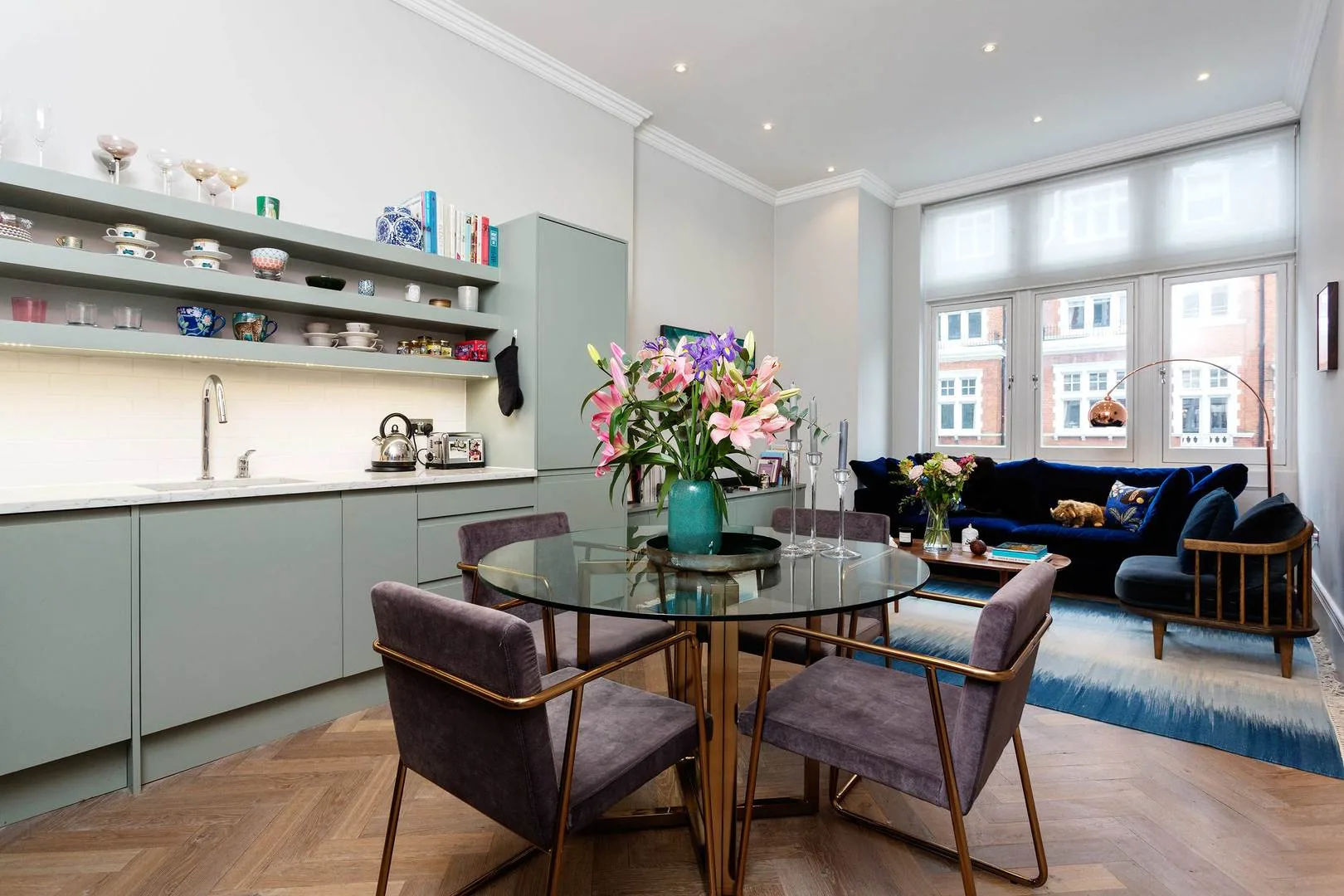 Una zona de comedor y estar con una mesa de vidrio y asientos junto a grandes ventanas.