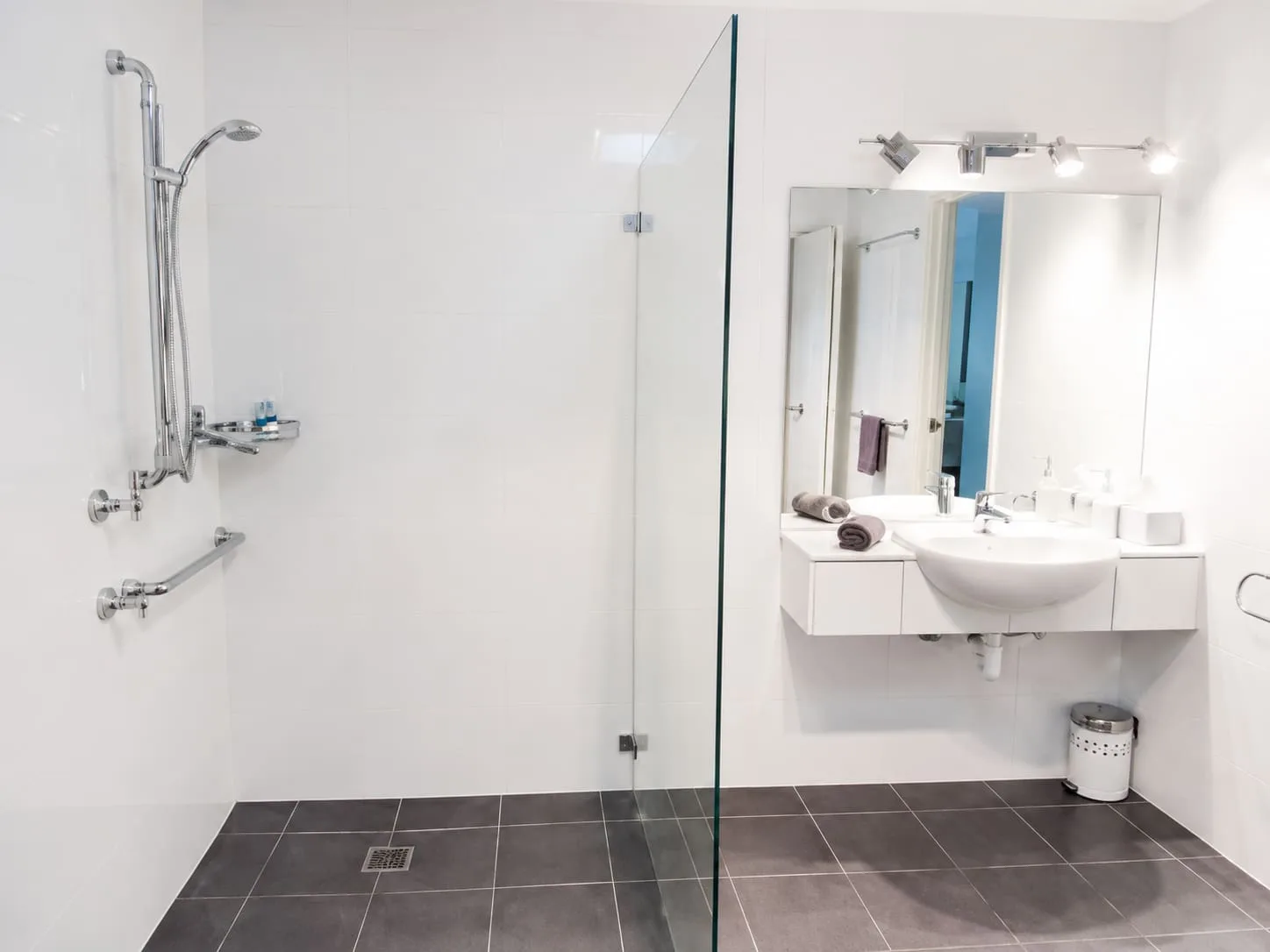 Un baño luminoso con una ducha de cristal y un lavabo suspendido.