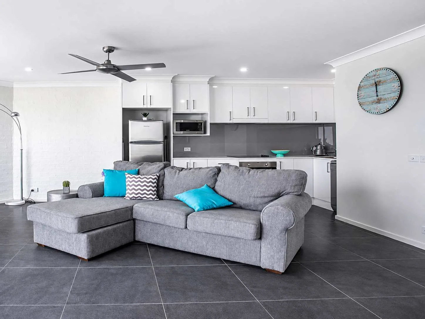 Sala de estar con asientos grises y una cocina abierta detrás.