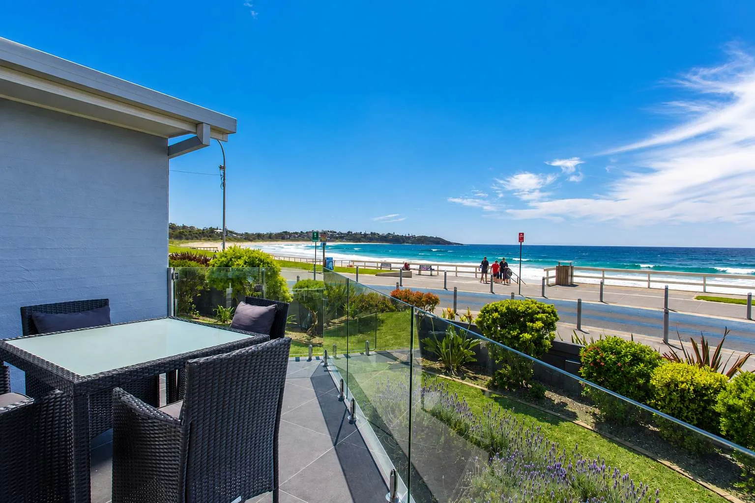 An outdoor patio with seating overlooks a beachfront promenade and ocean.