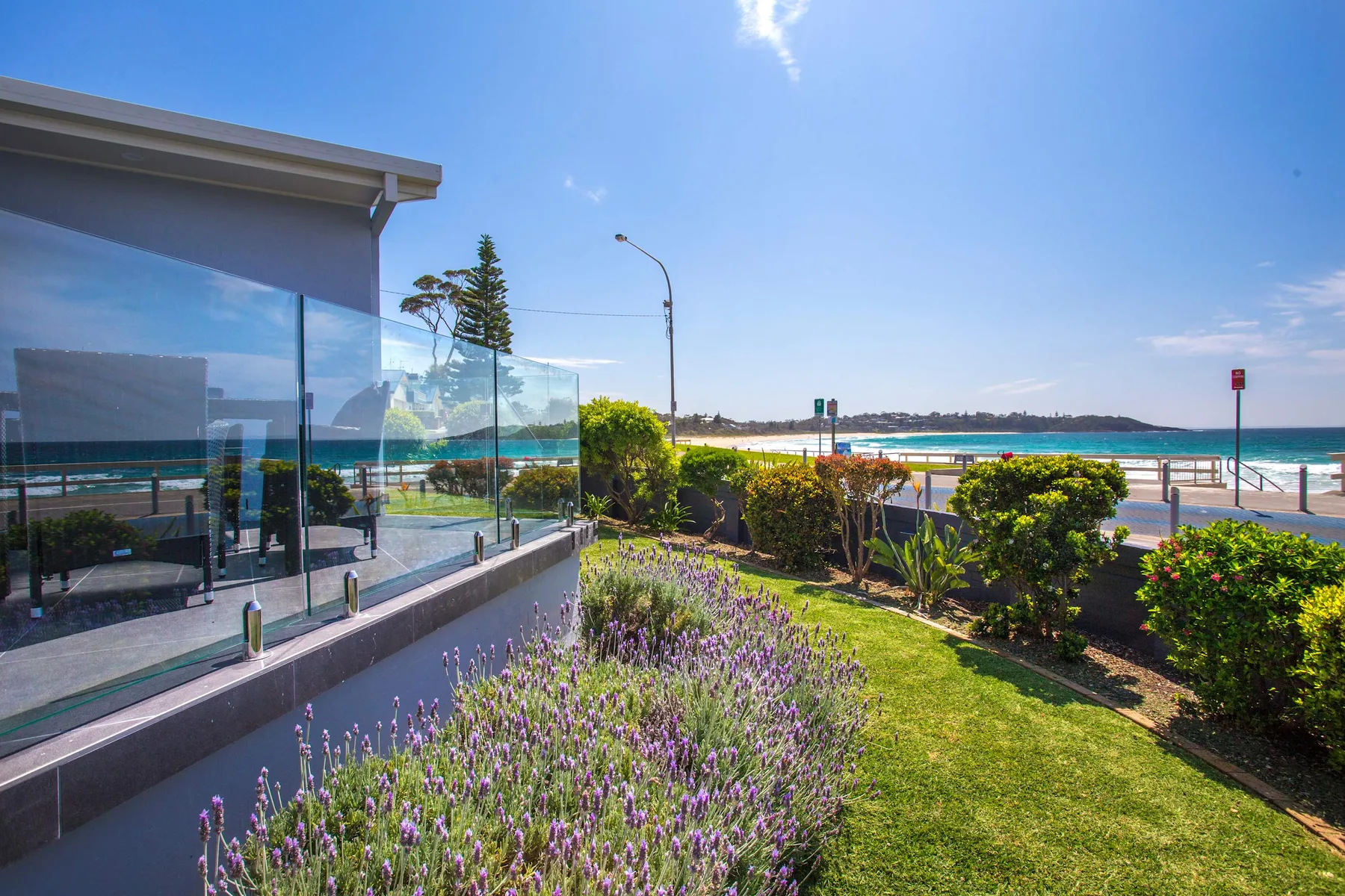 Un edificio con fachada de vidrio da a un jardín y una playa oceánica.