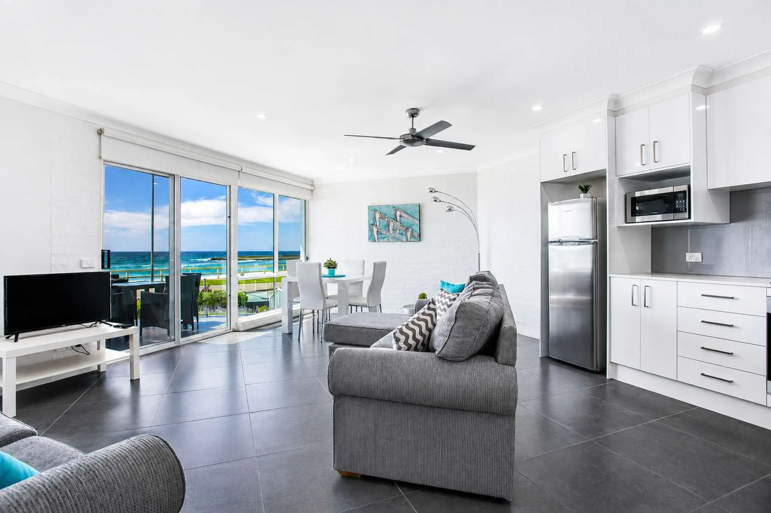 Bright living and dining area with seating beside large windows overlooking the ocean.