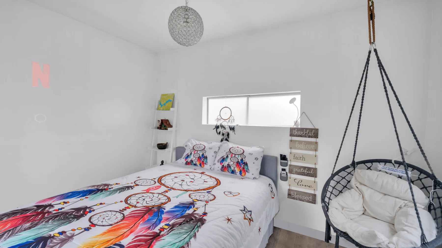 Un dormitorio colorido con una cama y una silla colgante junto a una ventana.