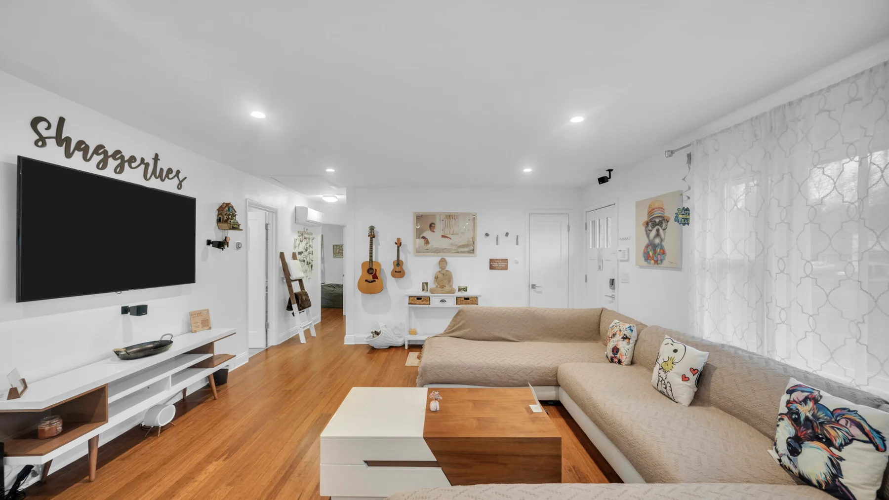 Una sala luminosa con sofá seccional, mesa de centro y televisor montado en la pared.
