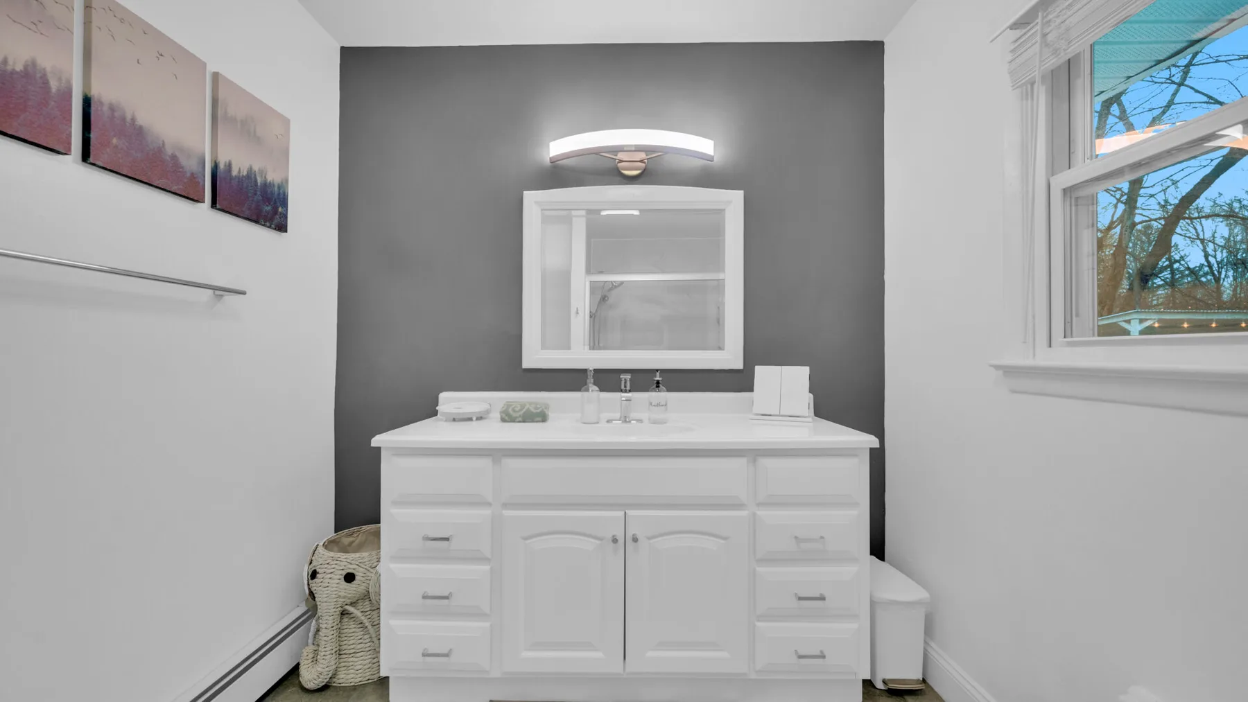 Un mueble de baño con espejo y luz de pared está frente a una pared gris.