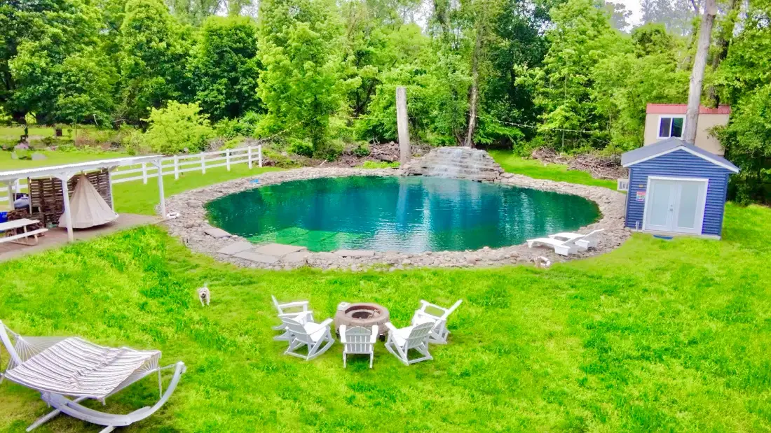 Una piscina exterior ajardinada ocupa un claro de césped rodeado de árboles.