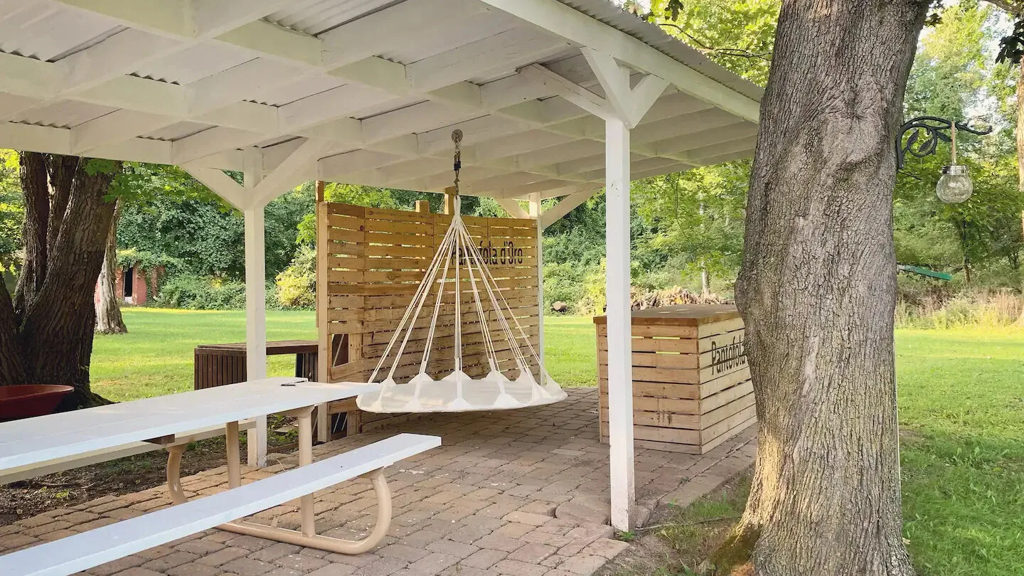 Una zona cubierta para sentarse al aire libre, con una silla colgante y mesas de picnic.