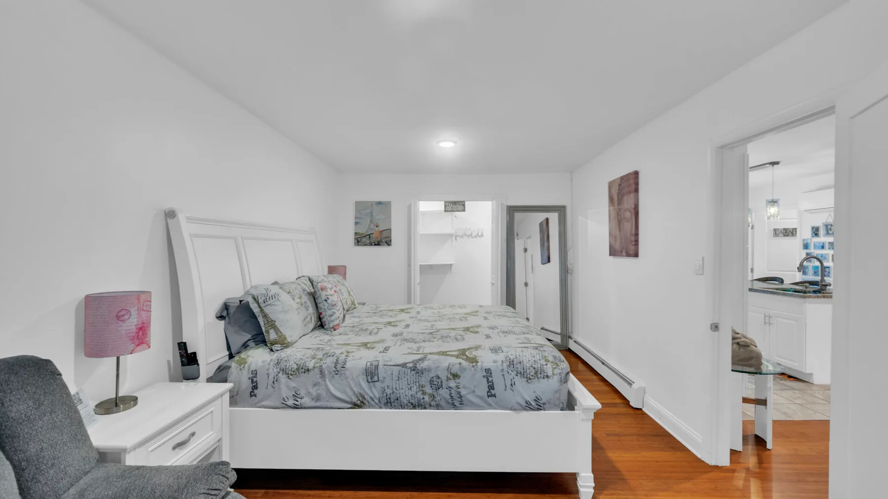 Un dormitorio con una cama, paredes blancas y suelo de madera cálida.