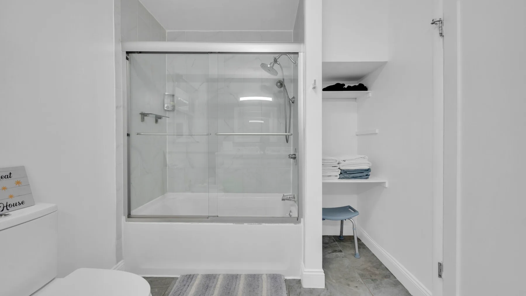 Un baño con una mampara de ducha de vidrio y estantes abiertos.