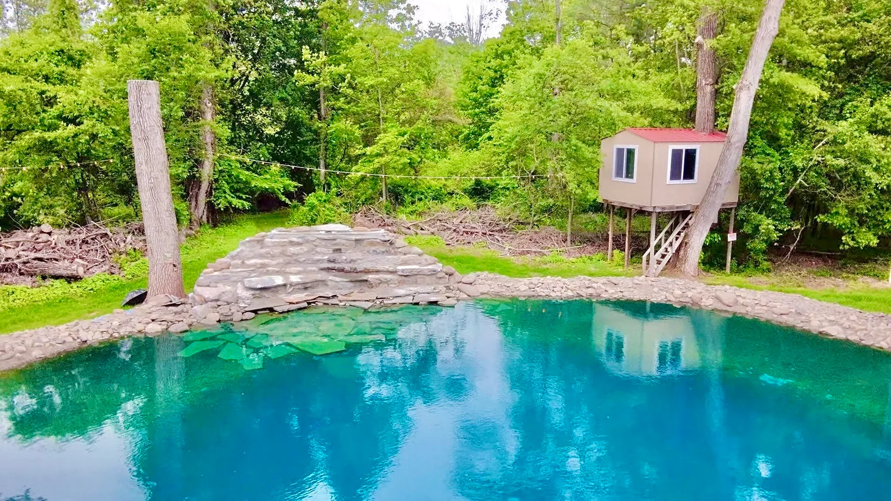 Una piscina de color azul verdoso está entre árboles, junto a una pequeña construcción elevada.