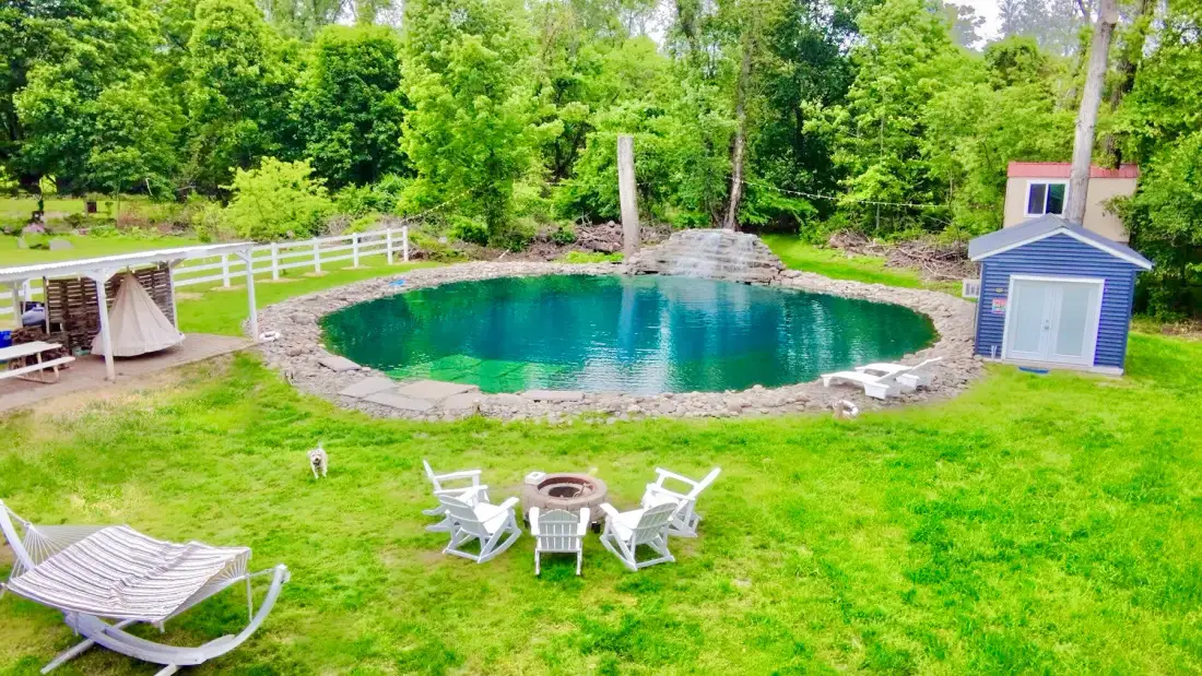 Un jardín presenta una piscina circular, asientos al aire libre y un pequeño cobertizo azul.