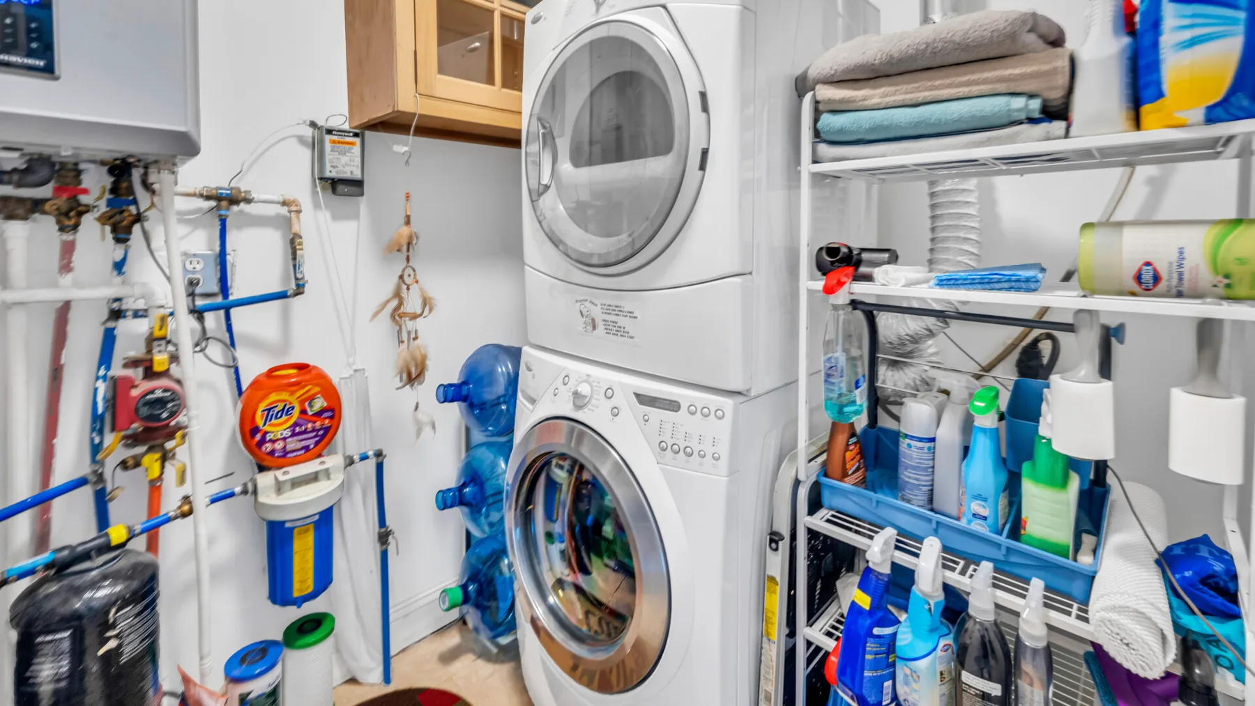 Un cuarto de lavandería y servicio con lavadora y secadora apiladas y estantes de almacenamiento.