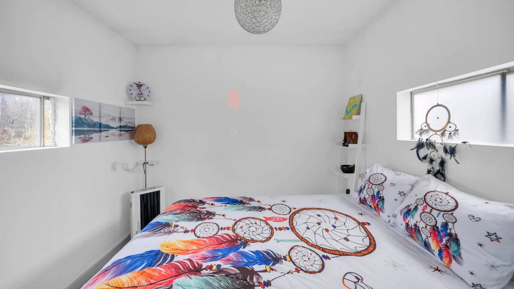 Un dormitorio luminoso con una cama cubierta de diseños coloridos de atrapasueños y plumas.
