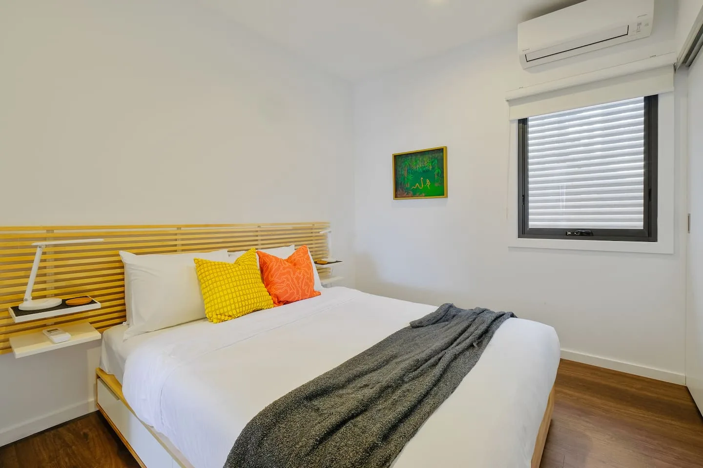 A bedroom with a neatly made bed, colorful pillows, and a window.
