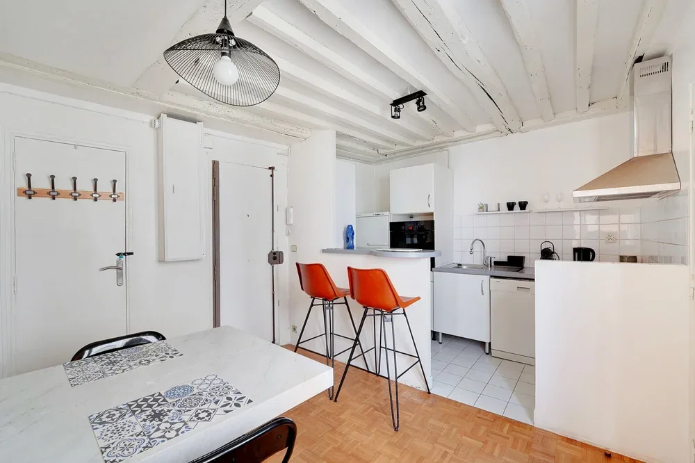 A bright kitchen and dining area with a table and orange stools.