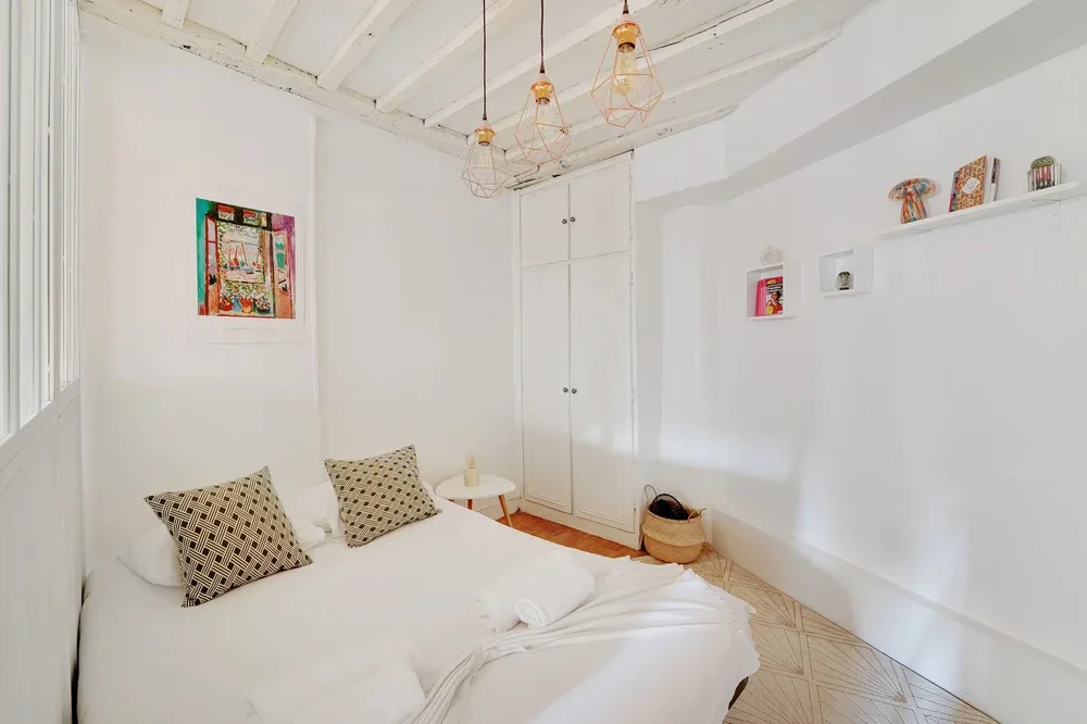 A bright bedroom with a bed, patterned pillows, and white walls.