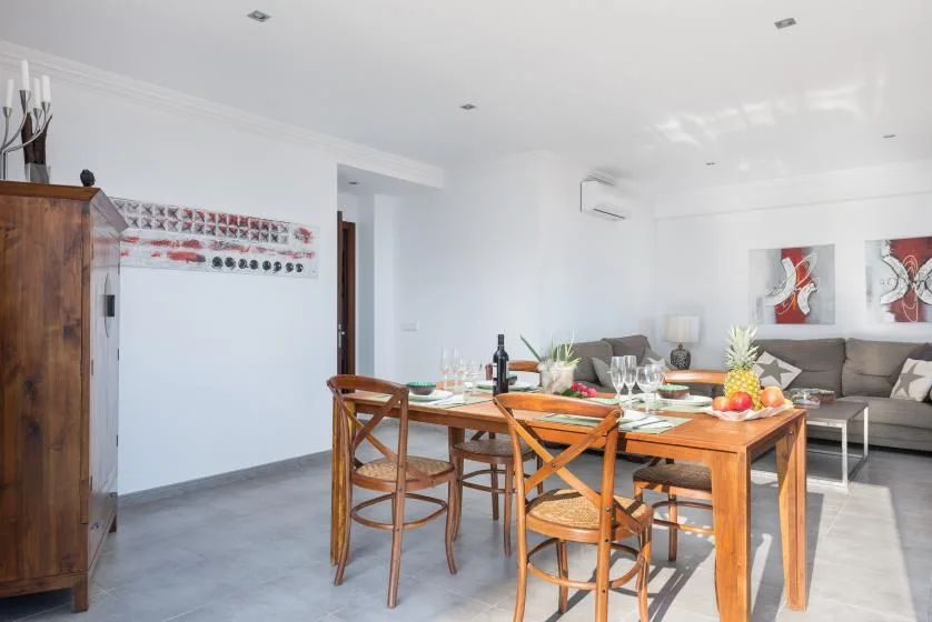 A bright open-plan dining and living area with a wooden table set for a meal.