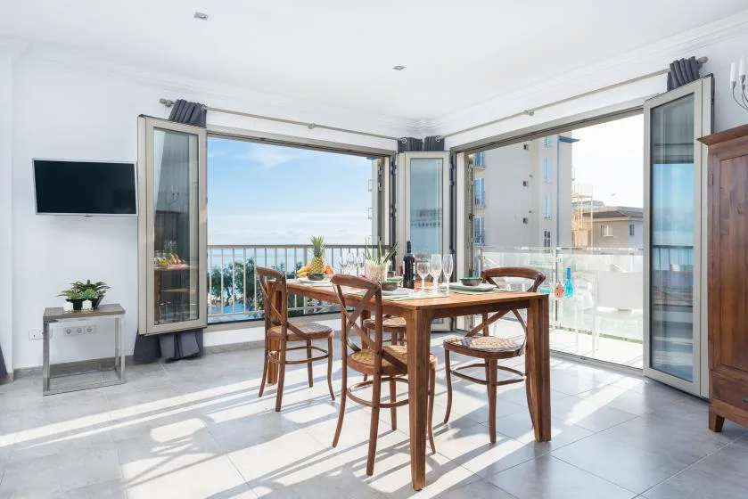 A bright dining area with a wooden table beside open glass doors and a balcony.