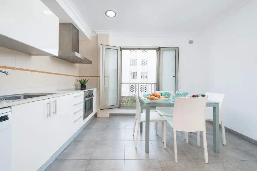 A bright kitchen and dining area with a table beside open balcony doors.