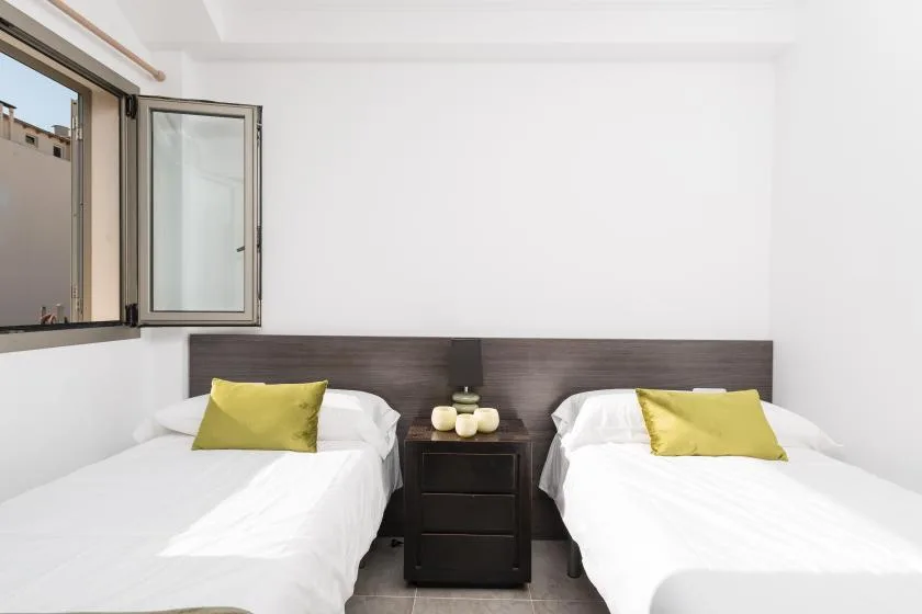 A bright bedroom with two beds and a nightstand between them.