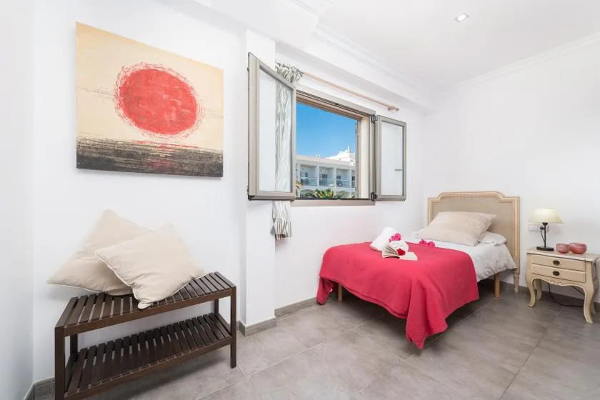 A bright bedroom with a bed dressed in a red cover and an open window.