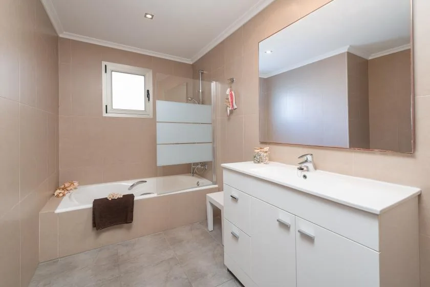 A tiled bathroom with a bathtub, shower, and white vanity beneath a large mirror.