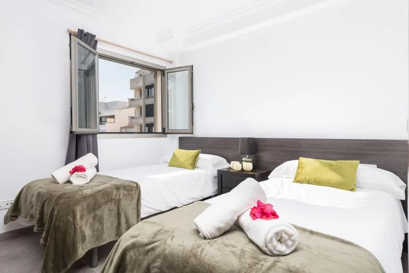 A bright bedroom with two beds and an open window.