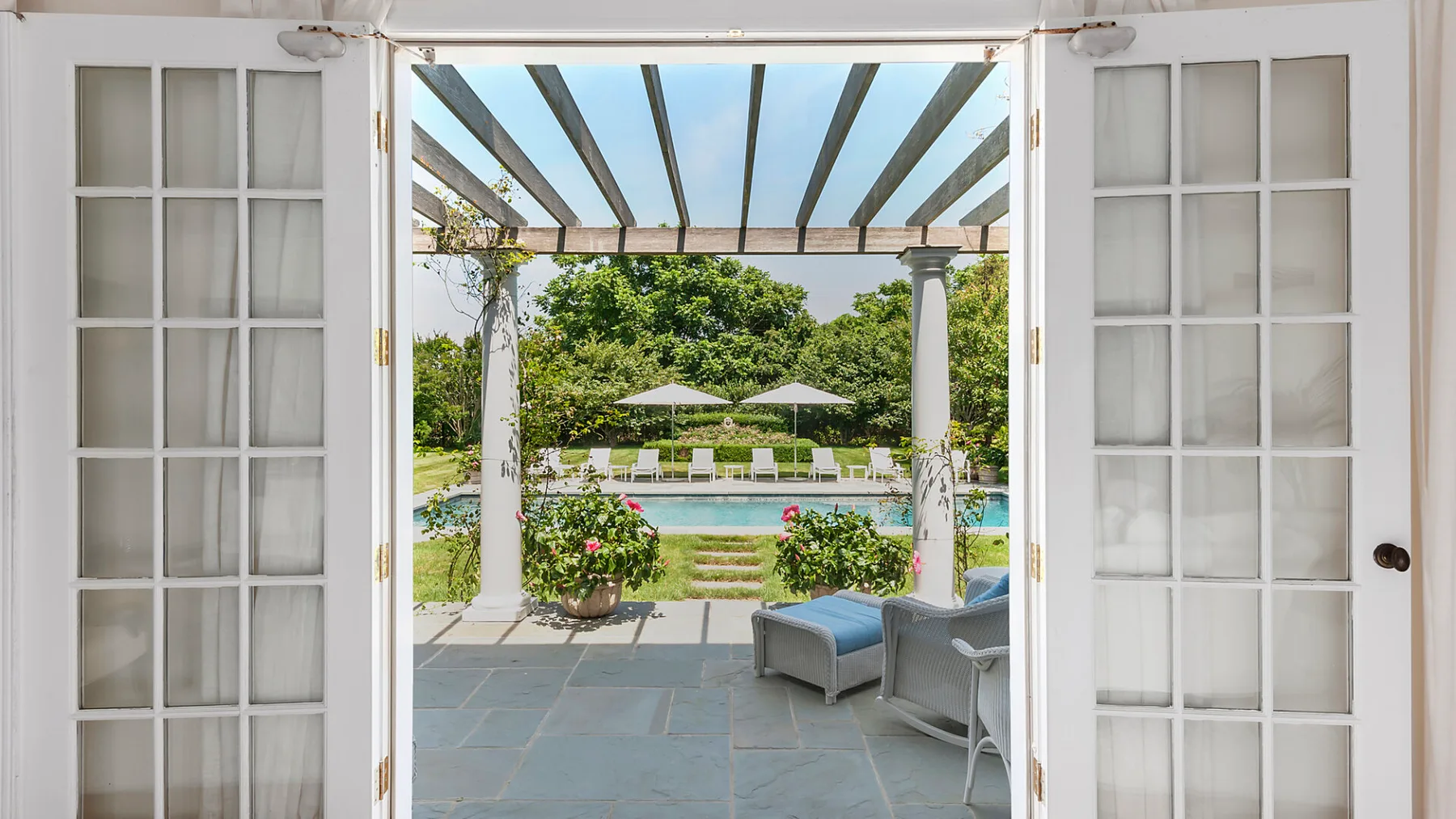 Una puerta abierta enmarca un patio con asientos, una piscina y una pérgola.