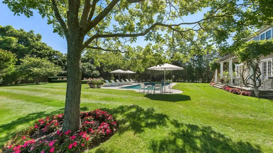 Un jardín ajardinado con piscina y asientos a la sombra.