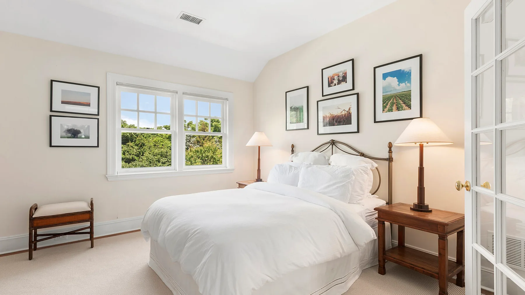 Un dormitorio luminoso con una cama blanca y ventanas con vistas a la vegetación.