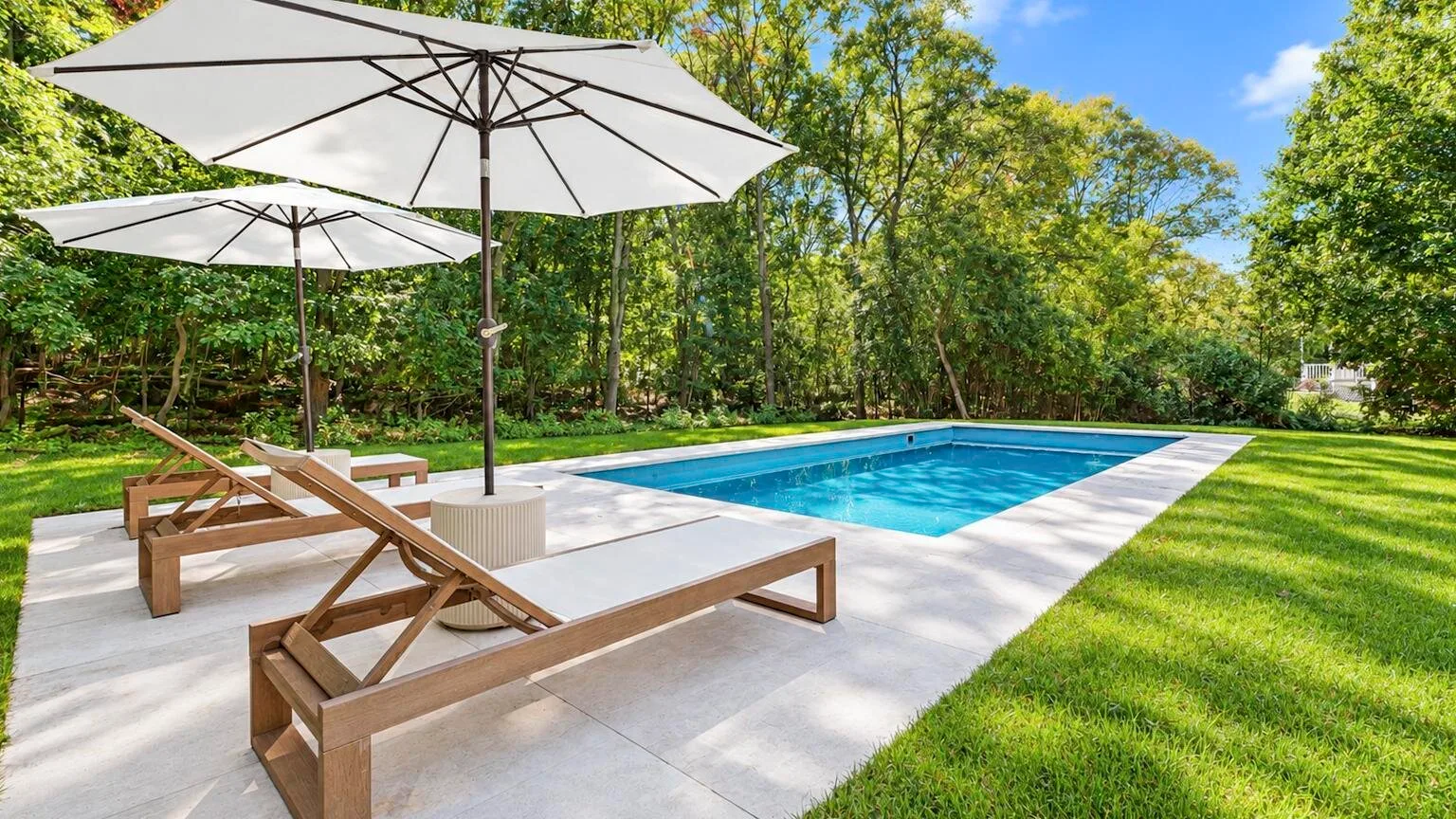 An outdoor swimming pool with loungers and umbrellas on a paved deck.