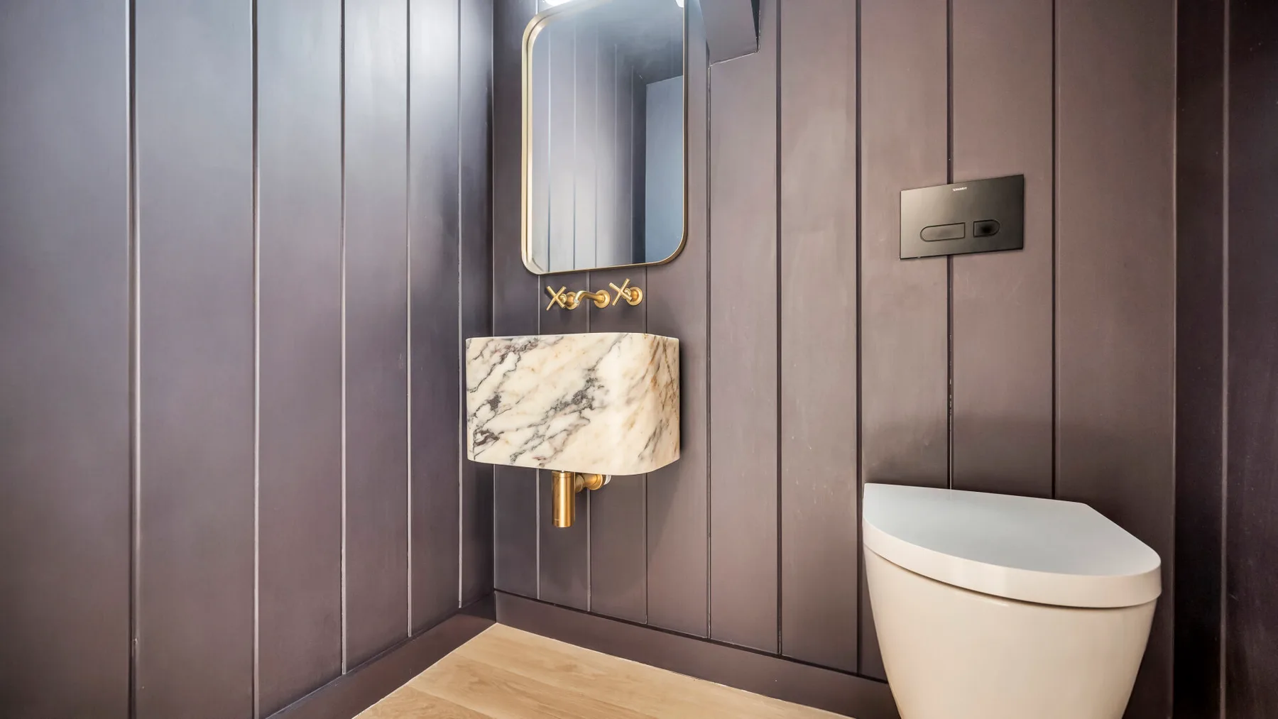 A bathroom with a wall-mounted sink and a toilet against paneled walls.