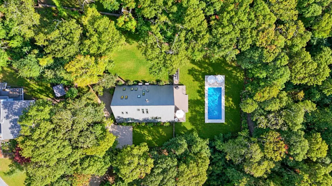 An aerial view shows a house and swimming pool surrounded by trees.