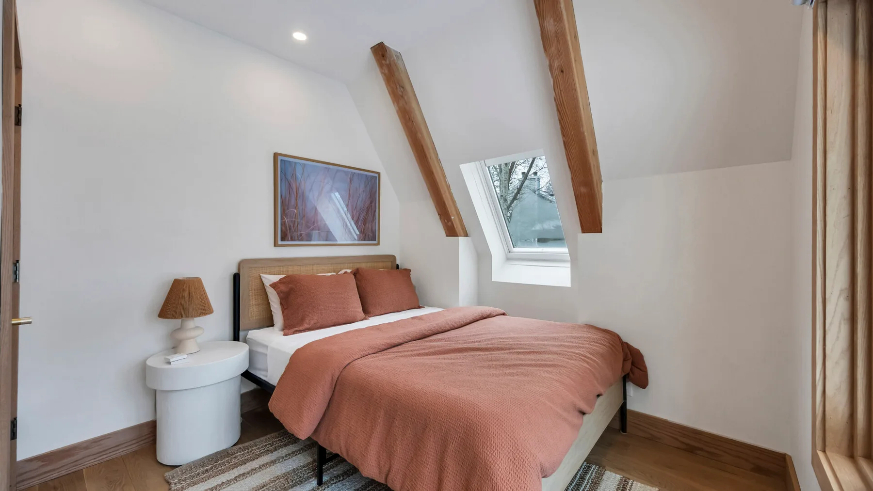 A bedroom with a bed dressed in rust-colored bedding beneath a sloped ceiling.
