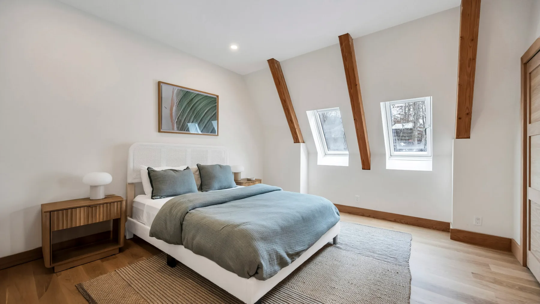 A bright bedroom with a bed beneath sloped ceilings and two windows.