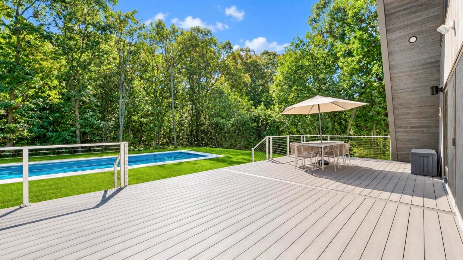 A spacious outdoor deck overlooks a swimming pool and surrounding trees.