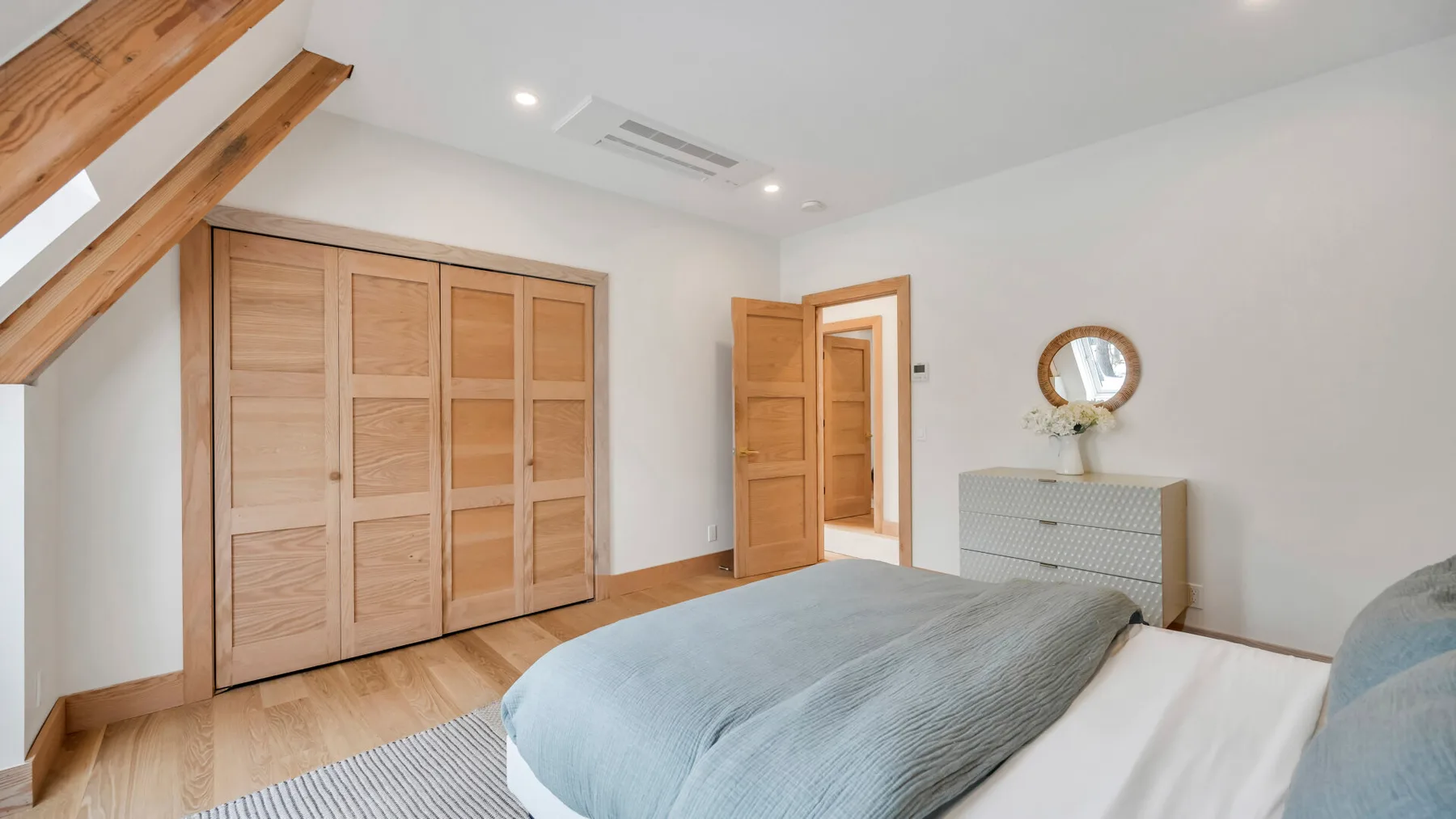 A bright bedroom with a bed, wooden wardrobe, and open doorway.