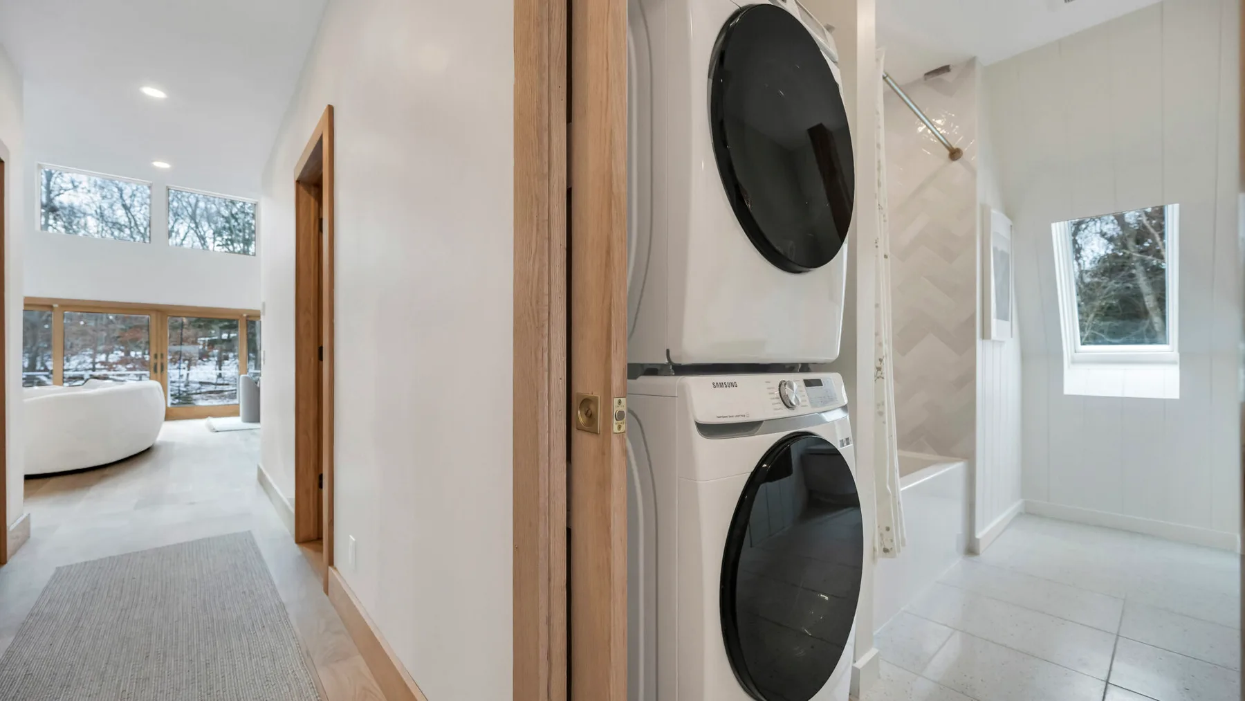 A bright hallway opens onto a bathroom with stacked laundry machines and a bathtub.