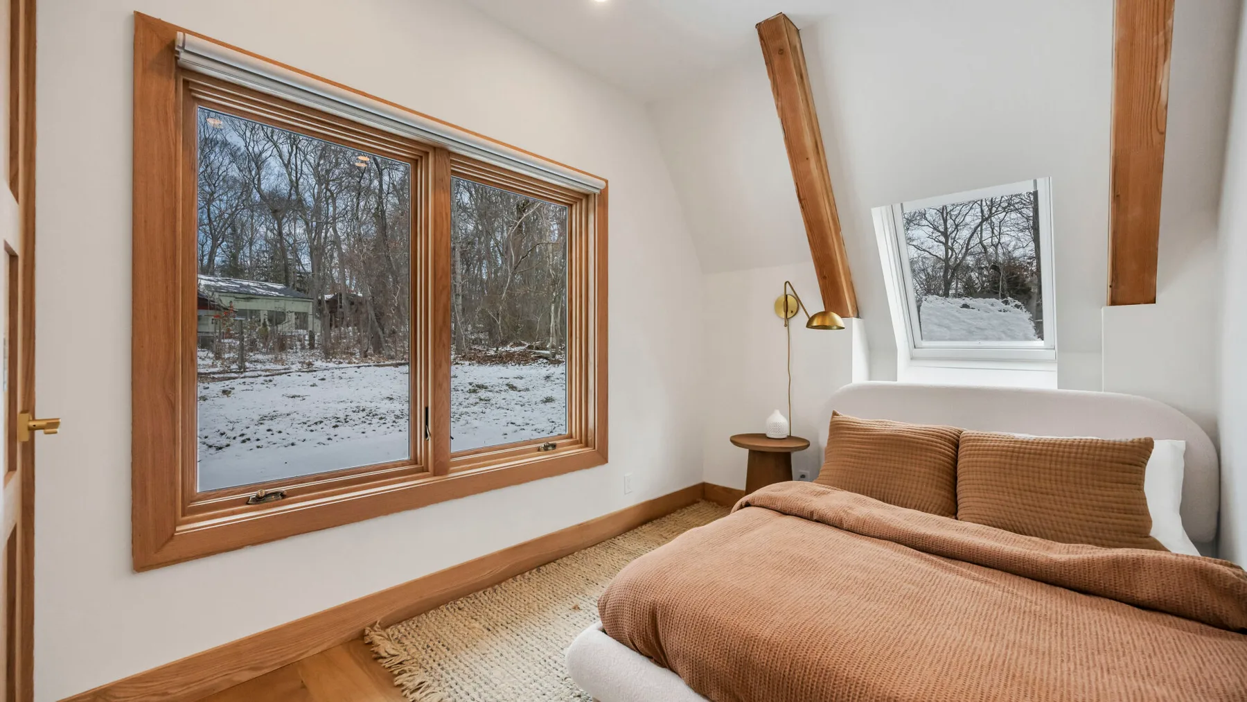 A bedroom with a bed beside large windows overlooking a snowy, wooded landscape.