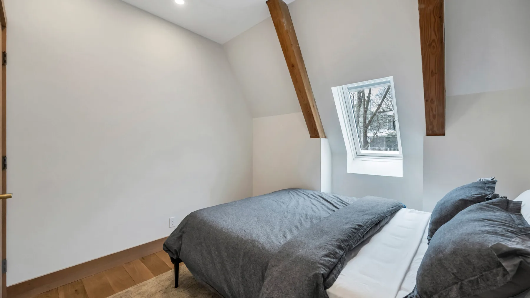 A sloped-ceiling bedroom with a bed beneath a small window.