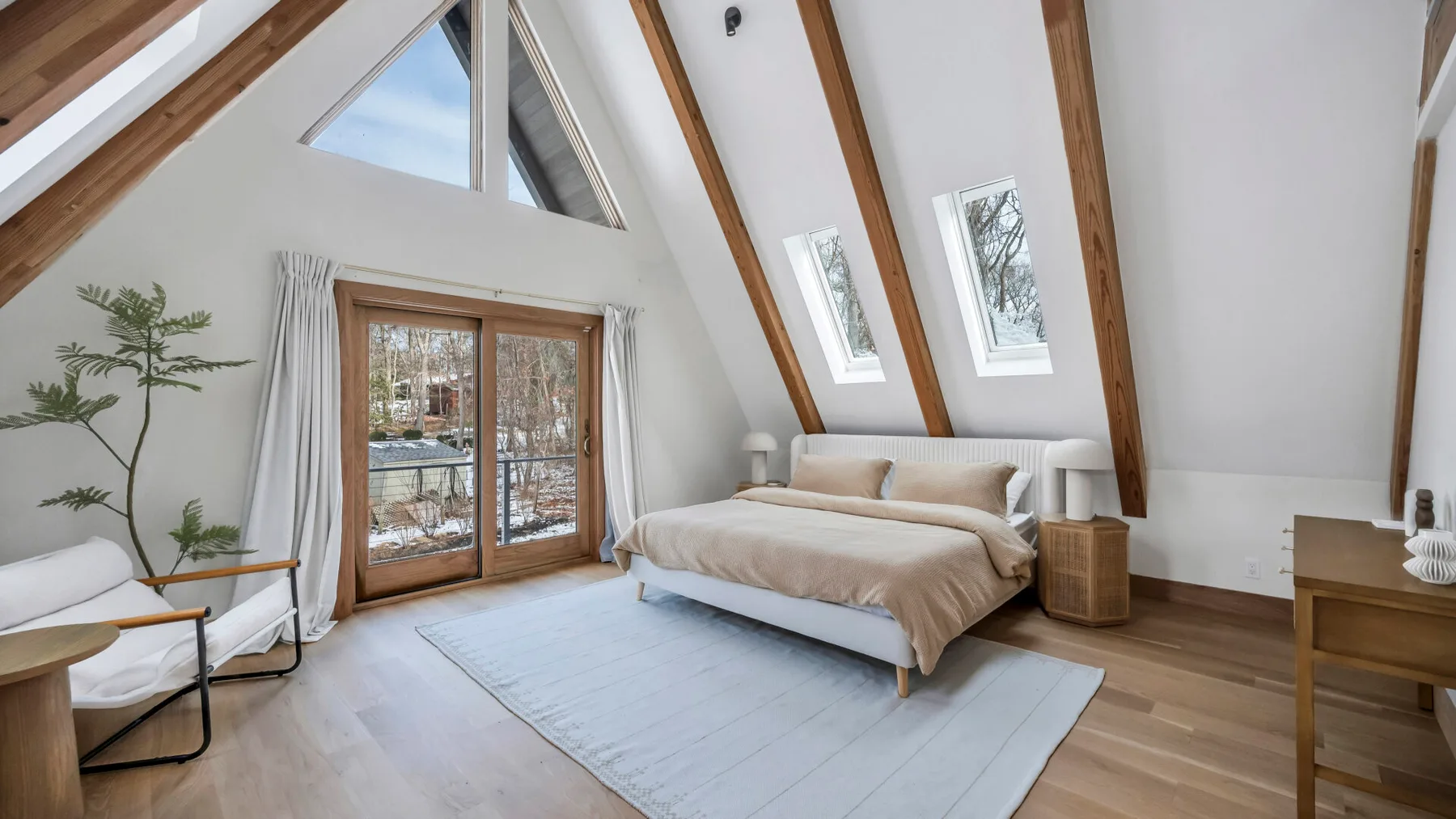 A bright attic bedroom with a bed beneath sloped ceilings and exposed beams.