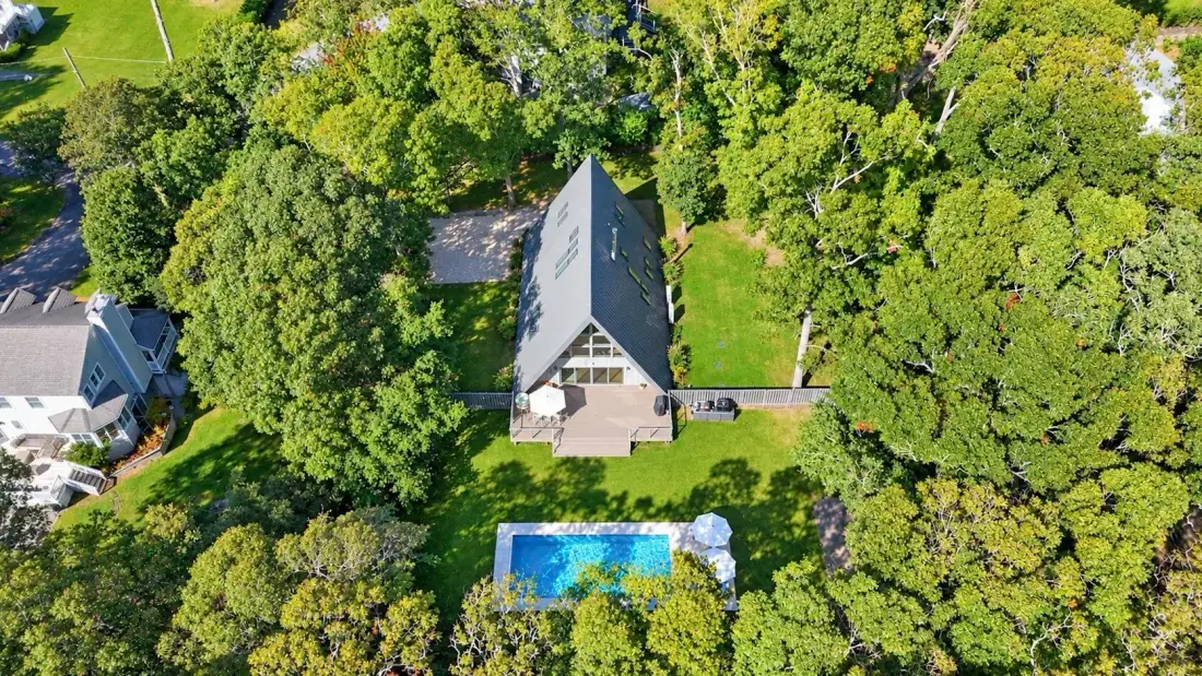 Aerial view of a house and blue swimming pool surrounded by trees.
