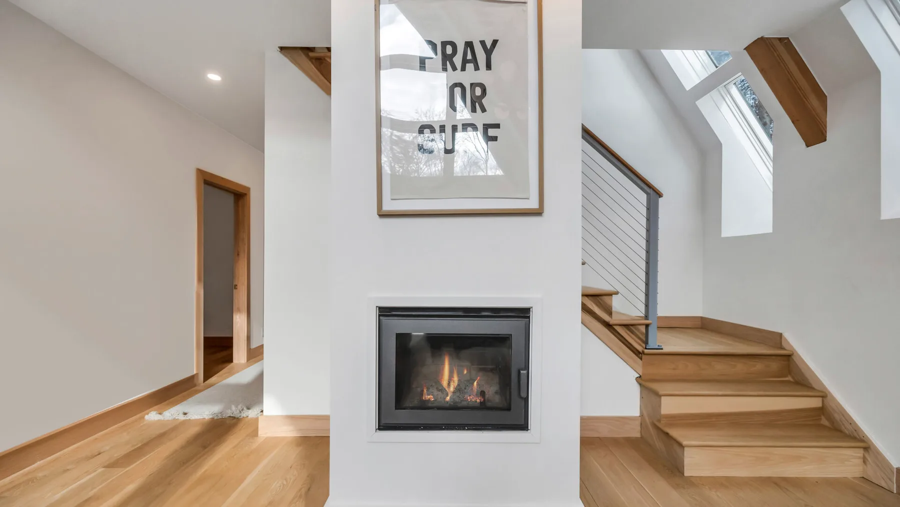 A bright interior hallway with a fireplace and wooden stairs.