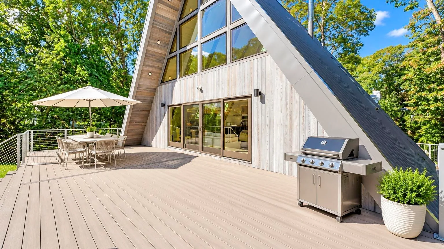 A-frame cabin exterior with a spacious deck, outdoor dining area, and grill.