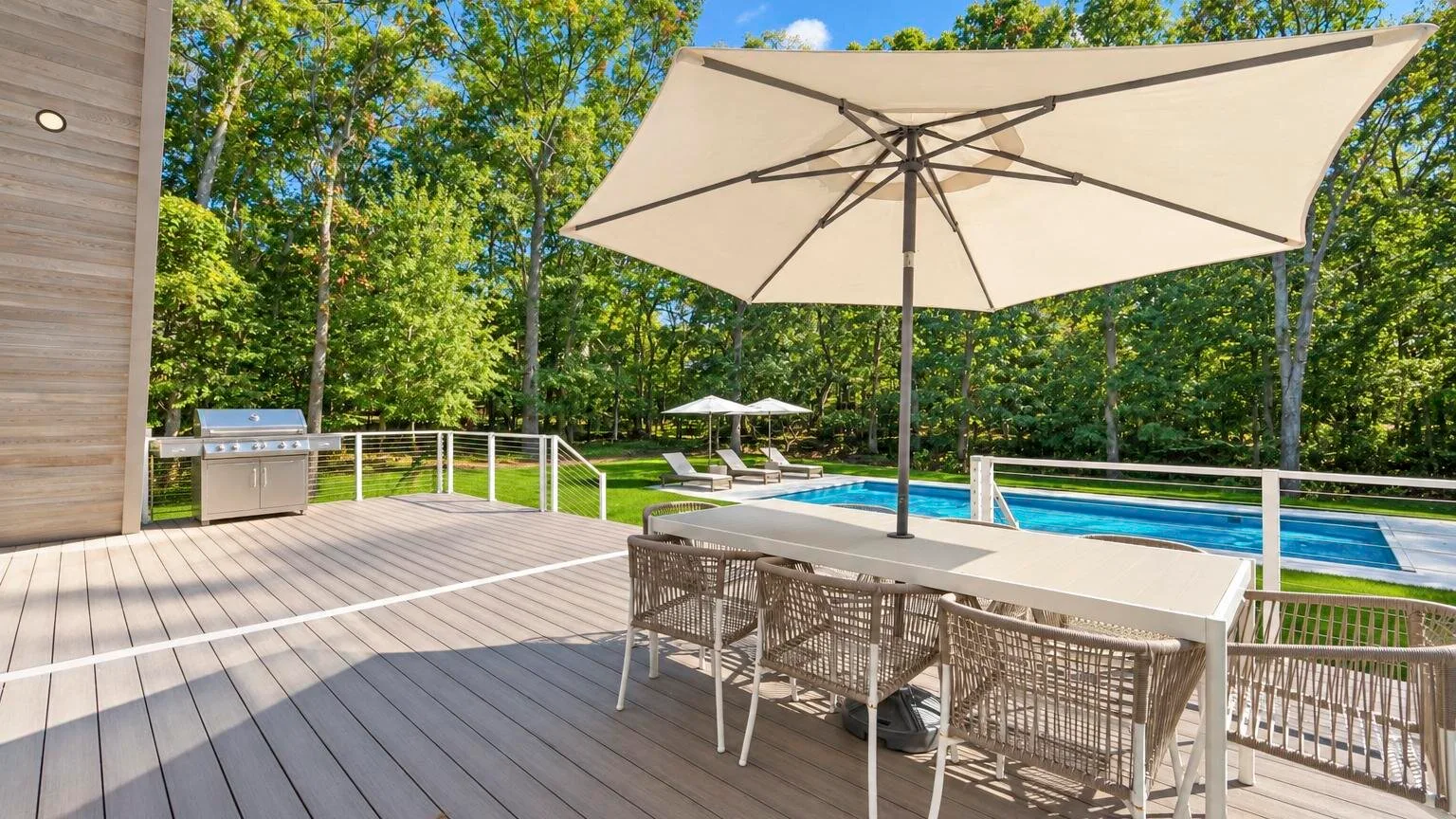 An outdoor dining area with a large umbrella overlooks a swimming pool.
